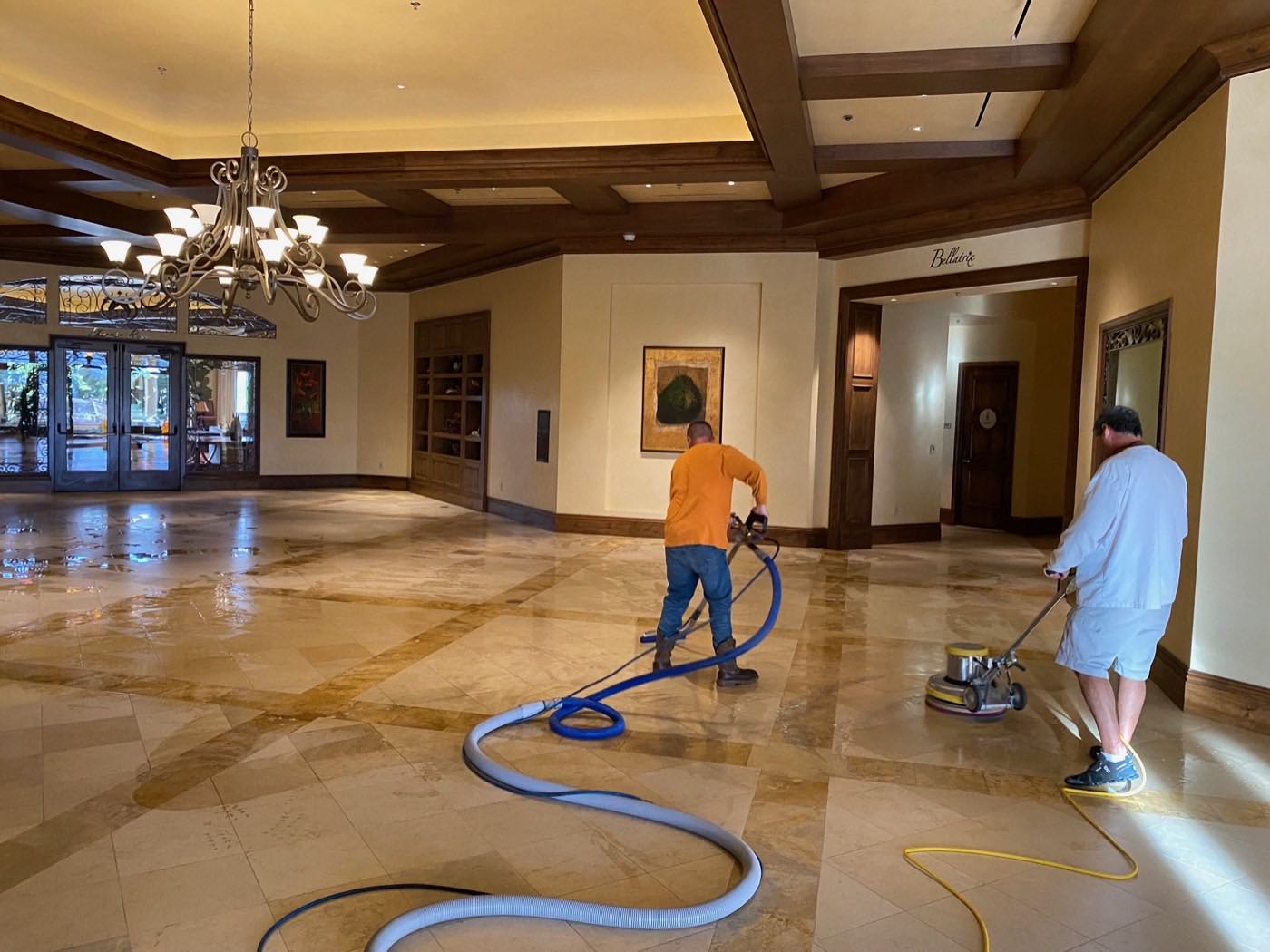 Team restoring travertine tile floors beneath the chandeliers of an elegant clubhouse