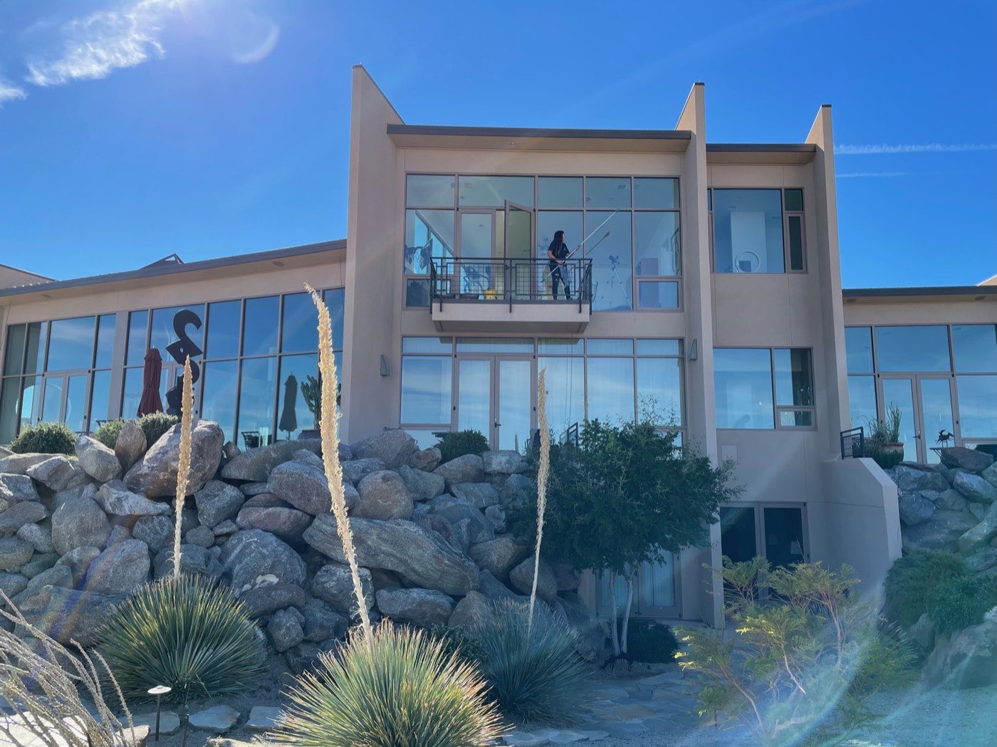 Palm Desert Window Cleaning technician working the tall glass of a hillside desert estate under a blue sky